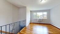 Located at 100 Rock Rd in Hawthorne, NJ, this thoughtfully designed space offers a clean, move-in-ready layout with consistent finishes throughout. Warm-toned hardwood flooring flows seamlessly across the living and bedroom areas, lending the space a cohesive and inviting character.

The open living area is a standout feature, anchored by an elegant wrought iron staircase railing with decorative scroll detailing. A wide window draws in generous natural light and offers views of the surrounding neighborhood greenery, while a wall-mounted air conditioning unit and baseboard heating ensure year-round comfort.

The kitchen is well-appointed with rich honey-toned wood cabinetry, granite-style countertops, and stainless steel appliances including a dishwasher. A large window above the kitchen area fills the space with natural light and overlooks lush outdoor greenery, creating a pleasant cooking environment.

The bedrooms continue the hardwood flooring theme and feature large windows that frame views of the tree-lined surroundings, along with baseboard heating for efficient climate control. The bathroom is finished in clean white tile with a window for natural ventilation, a vanity, and a full suite of fixtures, maintaining a bright and functional aesthetic throughout.