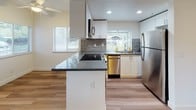 This single-level studio unit at Glenstone presents a clean, modern interior highlighted by warm wood-style plank flooring that runs throughout the open living area. The main living space is bright and open, benefiting from a large window that admits generous natural light and offers outdoor views. Crisp white walls and visible ceiling vents contribute to a fresh, well-maintained atmosphere. A ceiling fan is also present, adding to the unit's comfort.

The kitchen is a standout feature, equipped with stainless steel appliances including a refrigerator, dishwasher, range, and microwave. White shaker-style cabinetry pairs with a mosaic tile backsplash and dark countertops for a contemporary aesthetic. A peninsula with additional counter space and an integrated cooktop provides extra prep and storage functionality. Multiple windows in the kitchen bring in additional natural light.

Adjacent to the main living area, a dedicated walk-in closet offers built-in shelving and generous storage. The bathroom includes a full bathtub with tiled surround, finished in neutral tones. Recessed lighting in the kitchen and consistent flooring throughout unify the space into a cohesive, functional layout.