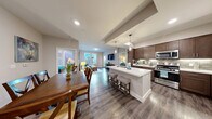 Located in Las Vegas, NV, this well-appointed 2-bedroom, 2-bathroom residence offers a thoughtfully designed single-level floor plan that maximizes both comfort and functionality. The open-concept living area seamlessly connects the kitchen, dining, and living spaces, creating an inviting atmosphere ideal for everyday living and entertaining. Rich wood-look flooring flows throughout the main areas, complementing the neutral, contemporary color palette.

The kitchen is a standout feature, outfitted with dark espresso cabinetry, a tile backsplash, stainless steel appliances including a gas range and microwave, and a white quartz-topped island with bar seating and pendant lighting overhead. The adjacent dining area comfortably accommodates a full-sized table and benefits from natural light filtering in through nearby windows.

The living room offers a relaxed setting with windows that frame outdoor views of lush landscaping. Both bedrooms are carpeted and generously proportioned, with the primary bedroom featuring a private en-suite bathroom and a walk-in closet with wire shelving. The bathrooms are finished with quartz countertops, dark cabinetry, and tub-shower combinations accented by mosaic tile inlays. Additional highlights include three closets, a hallway, a private balcony, and a dedicated laundry area.