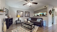 This single-floor residence offers a cohesive and thoughtfully designed layout across its key living areas. The living room serves as the heart of the home, anchored by a classic fireplace with a white mantel and complemented by wood-look flooring, a ceiling fan, and a pass-through shelf that connects to the kitchen. A decorative sunburst mirror above the mantel and framed artwork add personality to the neutral gray walls.

The galley-style kitchen is efficiently laid out with gray cabinetry, stainless steel appliances including a refrigerator, electric range, microwave, and dishwasher, all set over matching wood-look flooring. An open shelf above provides additional display and storage space.

The dining area is bathed in natural light from large windows dressed with layered blinds and teal curtains, creating an airy and welcoming space for meals.

The bedroom is a standout, featuring a rich teal accent wall, plush carpeting, a ceiling fan, and a window with light-filtering curtains. The room offers a calm and restful atmosphere.

The bathroom is clean and functional, with gray vanity cabinetry, a countertop sink, a tub-shower combination, and wood-look flooring throughout. Each space in this residence balances comfort and practicality with consistent, modern styling.