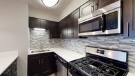 Located at 1075 Weybridge Rd in Columbus, Ohio, this single-floor residence offers a thoughtfully designed living space with modern finishes and functional details. The kitchen stands out as a highlight of the home, showcasing rich dark cabinetry with sleek hardware that creates a striking contrast against crisp white countertops. A mosaic tile backsplash in muted grays and whites adds texture and visual interest to the space. Stainless steel appliances, including a gas range, built-in microwave, and dishwasher, provide a cohesive, contemporary look while delivering practical utility. The undermount sink is positioned beneath task lighting, enhancing both functionality and ambiance. The kitchen's layout is efficiently organized to maximize storage and workspace, with upper and lower cabinetry providing ample room for essentials. The overall design aesthetic throughout reflects a modern sensibility, combining dark tones with lighter accents to create a balanced and inviting atmosphere. The single-floor layout ensures convenient, accessible living with all areas easily connected.