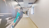 Located at 27 Park Rd in West Hartford, CT, this professionally designed fitness facility occupies a substantial single-floor footprint, offering a comprehensive workout environment organized across multiple distinct zones. The space features a clean, modern aesthetic throughout, with drop-panel ceilings fitted with linear LED lighting that provides consistent, bright illumination across all areas.

The main strength training floor is the centerpiece of the facility, housing an extensive array of selectorized machines and free weights arranged across durable, resilient flooring. Deep navy accent walls punctuate the space, complemented by a striking large-scale graphic mural featuring dynamic, flowing abstract lines that adds visual energy to the room. Mirrored walls enhance the sense of openness and support proper form monitoring.

A dedicated functional training area features a comprehensive multi-rack system stocked with kettlebells, resistance bands, medicine balls, and suspension trainers, alongside open floor space for movement-based exercises. Glass garage-style doors in this zone connect the interior to natural light and outdoor views.

A separate group exercise and cycling studio features warm hardwood flooring, floor-to-ceiling mirrors, wall-mounted screens, and glass partition walls. An additional open studio space accommodates group classes, equipped with a wall-mounted display and a varied collection of training accessories. A wide hallway adorned with large-scale athletic wall graphics connects the zones, reinforcing the facility's energetic, performance-focused atmosphere.