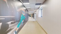Located at 27 Park Rd in West Hartford, CT, this professionally designed fitness facility occupies a substantial single-floor footprint, offering a comprehensive workout environment organized across multiple distinct zones. The space features a clean, modern aesthetic throughout, with drop-panel ceilings fitted with linear LED lighting that provides consistent, bright illumination across all areas.

The main strength training floor is the centerpiece of the facility, housing an extensive array of selectorized machines and free weights arranged across durable, resilient flooring. Deep navy accent walls punctuate the space, complemented by a striking large-scale graphic mural featuring dynamic, flowing abstract lines that adds visual energy to the room. Mirrored walls enhance the sense of openness and support proper form monitoring.

A dedicated functional training area features a comprehensive multi-rack system stocked with kettlebells, resistance bands, medicine balls, and suspension trainers, alongside open floor space for movement-based exercises. Glass garage-style doors in this zone connect the interior to natural light and outdoor views.

A separate group exercise and cycling studio features warm hardwood flooring, floor-to-ceiling mirrors, wall-mounted screens, and glass partition walls. An additional open studio space accommodates group classes, equipped with a wall-mounted display and a varied collection of training accessories. A wide hallway adorned with large-scale athletic wall graphics connects the zones, reinforcing the facility's energetic, performance-focused atmosphere.