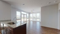 This single-floor residence is designed with an open-concept layout that seamlessly connects the kitchen, dining, and living areas. The kitchen serves as a central hub, featuring a large island with granite countertops, rich dark-wood cabinetry, a teal subway tile backsplash, and stainless steel appliances including an electric range and refrigerator. Built-in shelving near the kitchen provides additional storage and display space.

The living area is bright and airy, with hardwood-style flooring, recessed lighting, and a ceiling fan. A wall of windows and glass doors floods the space with natural light while offering outdoor views, creating an inviting and open atmosphere.

The bedrooms are carpeted for comfort, each equipped with ceiling fans and generously sized windows that bring in natural light and exterior views. The bathrooms are finished with the same dark cabinetry and granite countertops found throughout the unit, complemented by hardwood-style flooring, a tub-shower combination, and large mirrors above the vanities.

Consistent finishes, abundant windows, and a well-considered floor plan give this residence a cohesive, modern aesthetic with a bright, comfortable ambiance throughout.