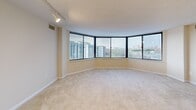 Located on the 15th floor at 3001 Park Center Dr in Alexandria, Virginia, this 2-bedroom, 3-bathroom residence offers a well-designed layout with an impressive sense of space and light throughout. The living room is a standout feature, anchored by a sweeping wall of floor-to-ceiling windows that wrap around the corner of the building, flooding the carpeted space with natural light and delivering expansive panoramic views of the Alexandria skyline and surrounding greenery. Track lighting accents the textured ceiling overhead. The generously sized primary bedroom also benefits from large windows with city views and includes an en-suite vanity area with a well-lit mirror. Both bedrooms feature soft carpeting, neutral tones, and ample natural light. The three bathrooms are clean and functional, with one featuring a full soaking tub and tiled flooring. The kitchen is efficiently laid out with white cabinetry, light countertops, tile flooring, and a convenient in-unit washer and dryer tucked alongside the appliances. A dedicated entrance and hallway connect the rooms cohesively. Two closets provide practical storage. The neutral color palette and carpeted floors throughout create a calm, move-in-ready atmosphere well-suited for comfortable urban living.