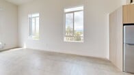 Located at 2735 E 6th St in East Los Angeles, this modern 1-bedroom, 1-bathroom loft-style unit spans two floors, offering a thoughtfully designed layout with contemporary finishes throughout. The main floor hosts an open-concept living and dining area distinguished by soaring ceilings and large windows that flood the space with natural light and frame views of the surrounding neighborhood, including glimpses of palm trees and the Los Angeles skyline. Polished concrete flooring runs throughout the main level, lending an industrial-modern aesthetic that complements the clean white walls.

The kitchen is efficiently designed with warm wood-tone cabinetry, light countertops, a white tile backsplash, a stainless steel sink, a built-in microwave, and an induction cooktop. An in-unit washer is seamlessly integrated beneath the counter, adding everyday convenience. The main floor also features soaring double-height ceilings, with a sleek black metal loft ladder providing access to the upper level.

The upper loft level serves as the private bedroom, offering a cozy retreat elevated above the main living area. The full bathroom is accessible on the main floor and features a glass-enclosed shower, grab bars, tile finishes, and polished concrete flooring. The overall design aesthetic is clean, minimal, and modern, making this a well-appointed urban residence.
