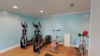 Located at 715 Rice Rd in Ridgeland, Mississippi, this dedicated fitness center is a well-appointed, single-floor space designed to support a comprehensive workout experience. The room is finished with warm hardwood-style flooring and painted in a calming light teal, creating an energizing yet welcoming environment. Crown molding runs along the perimeter, adding a polished architectural touch, while recessed lighting ensures the space is well-lit throughout.

Large, multi-pane windows along one wall allow abundant natural light to fill the room and offer views of the surrounding greenery, enhancing the overall atmosphere. The fitness center is equipped with multiple elliptical machines, a treadmill, a stationary air bike, a spin bike, a power tower for bodyweight training, and a dumbbell rack, providing a well-rounded selection of cardio and strength training options. A workout bench adds further versatility for strength exercises.

A central structural column divides portions of the room while maintaining an open flow, and a fire extinguisher is conveniently mounted for safety. Signage designates the space as a fitness center, reinforcing its dedicated purpose. Ventilation is provided through ceiling vents, ensuring comfort during exercise. Overall, this fitness center is a functional and thoughtfully finished space suited for daily fitness routines.