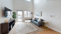 Located at 1005 W Fifth Ave in Columbus, Ohio, this two-bedroom, three-bathroom two-story residence offers a thoughtfully designed layout spread across two floors. The main level is anchored by an open-concept kitchen and living area distinguished by soaring ceilings that flood the space with natural light. The kitchen features dark espresso cabinetry, stainless steel appliances, a subway tile backsplash, and a large granite-topped island with bar seating — ideal for both cooking and casual dining. Warm hardwood-style flooring runs throughout the main level, and a glass door leads to a private balcony with outdoor views. The living area benefits from dramatic ceiling height and large windows, enhancing the sense of openness. The upper floor includes two well-proportioned bedrooms with plush carpeting and generous natural light. The primary bedroom includes a spacious walk-in closet with wire shelving systems. The bathrooms are finished with granite countertops, dark wood vanities, and tiled surrounds. A versatile loft overlooks the main level and is served by a ceiling fan. Additional features include a dedicated laundry area, two staircases, and ample utility and storage spaces throughout.