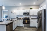 This single-floor, 2-bedroom, 2-bathroom residence in Clarksville, Indiana, offers a thoughtfully designed layout with modern finishes throughout. The open-concept kitchen is a standout feature, showcasing white shaker cabinets, granite countertops, a subway tile backsplash, and a full suite of stainless steel appliances, including a range, microwave, dishwasher, and refrigerator. A kitchen island with a built-in sink provides additional prep space, while pendant lighting adds a stylish touch. The kitchen flows seamlessly into the dining and living areas, which are finished with warm hardwood-style flooring. The living room is bright and inviting, featuring French doors that let in natural light and provide outdoor access. Both bedrooms are carpeted for comfort and include windows that bring in natural light. The bedrooms are served by well-appointed bathrooms, one of which features hardwood-style flooring, a walk-in shower, and a granite-topped vanity. A spacious walk-in closet with wire shelving provides generous storage. A dedicated laundry area with washer and dryer hookups adds everyday convenience, completing this functional and stylish home.