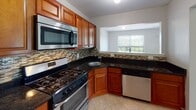 Located in Somerset Park in Franklin Park, NJ, this two-bedroom, two-bathroom residence offers a well-designed single-floor layout that balances comfort and functionality. The open-concept living and dining area is spacious and carpeted, featuring a distinctive built-in pass-through shelf that connects to the adjacent space, adding architectural character to the neutral, light-toned interior. The kitchen is a standout feature, outfitted with warm cherry wood cabinetry, dark granite countertops, a mosaic tile backsplash, and stainless steel appliances including a gas range, built-in microwave, and dishwasher. Tile flooring and a window overlooking the outdoors complete the kitchen's bright, functional design. Both bedrooms are generously sized with plush carpeting and windows that invite natural light. The primary bedroom includes direct access to a full en-suite bathroom and a closet. The en-suite bath features a tub-shower combination with sliding glass doors, a vanity with wood cabinetry, and tile flooring. The second full bathroom is clean and classic, with white tile wainscoting and a mirrored medicine cabinet. Throughout the unit, neutral gray walls provide a versatile backdrop suited to a variety of décor styles.