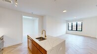 Located at 100 East Putnam Avenue in Greenwich, CT, this thoughtfully designed one-bedroom, one-bathroom residence offers a refined living experience with high-end finishes throughout. The open-concept living, dining, and kitchen area serves as the heart of the home, showcasing stunning herringbone-patterned hardwood floors, crisp white walls, and abundant natural light through black-framed windows. The chef's kitchen is a standout, featuring a large waterfall-edge marble island with an undermount sink and brushed gold faucet, rich walnut cabinetry extending to the ceiling, a marble tile backsplash, and premium stainless steel appliances with gold accents. A versatile den provides additional flexible living space. The bedroom is a serene retreat with light hardwood floors, a black-framed window with outdoor views, and access to multiple well-organized closets with built-in shelving systems. The bathroom is elegantly appointed with full-wall square ceramic tile, a floating walnut vanity topped with marble, gold fixtures, an arched mirror, and a soaking tub. A utility room and hallway complete the efficient, well-planned layout of this polished Greenwich residence.