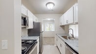 This single-floor residence offers a thoughtfully laid-out living space with a clean, neutral aesthetic throughout. The galley-style kitchen is a standout feature, showcasing white shaker cabinetry, marble-patterned countertops, and a full suite of stainless steel appliances including a refrigerator, electric range, over-the-range microwave, and dishwasher. Light tile flooring runs underfoot, and a window at the end of the kitchen draws in natural light while offering a view of the surrounding greenery. The kitchen opens conveniently into the main living area, which is finished with plush carpeting and features a sliding glass door fitted with vertical blinds that provide access to an outdoor view. An additional window further brightens the space. The bedrooms are generously sized, each carpeted and bathed in natural light from wide windows. Closet space is available, and the neutral wall tones lend a calm, versatile backdrop. The bathroom is clean and functional, featuring a full tub and shower combination with white tile surround, a grab bar, and tile flooring in a warm taupe tone. Throughout the residence, the consistent use of soft neutral tones and natural light creates a bright, comfortable, and move-in-ready atmosphere.