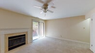This single-story residence offers a well-organized layout with a practical flow between its main living areas. The living room serves as the central gathering space, finished with wall-to-wall carpet in a neutral beige tone and painted in soft, warm hues throughout. A tile-surround fireplace with a white decorative mantel anchors one wall, while a large sliding glass door fitted with vertical blinds opens to an outdoor balcony, allowing natural light to fill the room. A ceiling fan with a light fixture is centrally mounted overhead, providing both ventilation and ambient lighting.

The kitchen is efficiently arranged, featuring light wood cabinetry, tile backsplash, and light-toned flooring. It is equipped with a stainless steel refrigerator, black dishwasher, electric range, and a stainless sink positioned beneath a window. The bathroom includes a white vanity with an integrated sink, overhead lighting, a wall-mounted storage cabinet, and a shower-tub combination with a glass door.

An additional carpeted room, also equipped with a ceiling fan and a window, provides flexible use as a bedroom or office. Throughout the space, consistent neutral finishes and ample natural light contribute to a clean, understated ambiance.