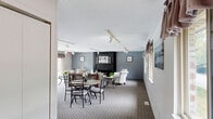Located at 37140 S Orchard Cir in Westland, Michigan, this single-floor community space offers a well-organized and welcoming layout designed for comfort and social gathering. The open-concept living and dining area forms the heart of the space, bathed in natural light from multiple windows adorned with brown valance curtains and a large sliding glass door that frames a direct view of the outdoor pool area — a standout feature that brings a resort-like quality to the interior.

The living area is anchored by a bold, dark-framed fireplace set against a cool blue-grey accent wall, creating a warm focal point for gathering. Track lighting runs throughout the ceiling, providing flexible, adjustable illumination across the carpeted floors. The textured ceiling adds a classic touch consistent with the overall design.

The dining area flows naturally from the living space, offering a seamless transition that supports easy movement and interaction. Nearby, the kitchen is equipped with stainless steel appliances, including a full-size refrigerator and microwave, alongside dark cabinetry and countertops — practical and efficiently arranged. Overall, the space presents a clean, functional, and inviting atmosphere suited for community use and social events.