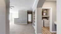 This single-story, 3-bedroom, 2-bathroom home offers a practical and modern layout designed for comfortable everyday living. The open-concept kitchen and living area serves as the heart of the home, where the kitchen stands out with white shaker cabinetry, a grey subway tile backsplash, white quartz countertops, stainless steel appliances, and light hardwood-style flooring. A peninsula with a built-in sink provides additional prep space and casual seating. The adjoining living room features plush carpet, crown molding, a ceiling fan, and built-in shelving framed by a distinctive arched entryway that adds architectural character. Each of the three bedrooms is finished with soft carpet and neutral grey walls, with windows that allow natural light to fill the rooms. The generously sized primary bedroom includes a walk-in closet with wire shelving. Both bathrooms are finished consistently with white vanities, quartz countertops, large mirrors, tub-shower combinations, and light wood-look vinyl flooring. A dedicated laundry area with a full-size washer and dryer is accessible off the main living space, alongside a water heater. Two hallways connect the layout efficiently, creating a smooth flow throughout the home.