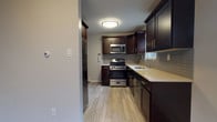 This multi-level residence spans three floors, offering a thoughtfully designed layout with a blend of updated finishes and practical living spaces throughout. The kitchen is a standout feature, showcasing rich dark espresso cabinetry with brushed gold hardware, light quartz countertops, a gray tile backsplash, and a full suite of stainless steel appliances including a gas range, microwave, refrigerator, and dishwasher. Light wood-look tile flooring grounds the kitchen with a clean, modern aesthetic. The living areas are highlighted by gleaming hardwood floors in warm tones, recessed lighting, and large windows that allow generous natural light to fill each room. A staircase with decorative iron railings connects the floors, adding a classic architectural touch. The bedrooms are comfortably sized, each featuring hardwood floors, ample closet space with double-door closets, and wall-unit climate control. The bathroom is finished with white subway tile wainscoting, an accent band of gray tile, a dark vanity with a white basin, and chrome fixtures. The lower level provides a spacious utility basement with a washer and dryer, painted concrete floors, and small windows for ventilation — offering practical storage and laundry functionality.