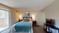 Located on Fifth St W in Palmdale, California, this single-story unit offers a practical and comfortable layout designed to maximize functionality. The living and sleeping area serves as the focal point of the space, highlighted by a wood-paneled fireplace that adds a warm, rustic character to the neutral-toned interior. Soft carpeting underfoot and vertical blinds leading to a sliding glass door with outdoor views contribute to a relaxed ambiance throughout this area. A ceiling fan provides additional comfort.

The kitchen is efficiently designed with light wood cabinetry, a gas range, built-in microwave, and a full-size refrigerator. A peninsula with a dark countertop separates the kitchen from the adjoining dining area, creating an open, connected feel. Overhead panel lighting brightens the workspace effectively. Tile flooring runs through the kitchen and entry areas, transitioning to carpet in the living and sleeping spaces.

The bathroom features a tub and shower combination with a decorative curtain, tile flooring, and a vanity with mirror. Neutral walls and clean lines give it a simple, functional appeal. Overall, the space presents a straightforward, well-maintained interior suited for everyday living in the Palmdale area.