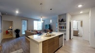 This well-appointed 2-bedroom, 2-bathroom residence is thoughtfully designed on a single floor, offering an open-concept layout that seamlessly connects the kitchen, dining, and living areas. The kitchen serves as a central hub, featuring a large island with a white quartz countertop, an undermount sink, and warm wood-toned cabinetry. A dishwasher is integrated beneath the island, and stylish pendant lights hang overhead, adding a contemporary touch.

The open flow leads directly into the living area, which is bathed in natural light from large windows fitted with blinds. The space is anchored by hard surface flooring throughout, lending a clean and cohesive aesthetic. A built-in shelving unit adds both functional storage and a decorative focal point to the living room, ideal for displaying personal items.

The layout provides a comfortable sense of scale without feeling overwhelming, making efficient use of every area. The neutral color palette of soft whites and warm wood tones creates a welcoming and modern ambiance. Access to an outdoor area is visible through the sliding glass door, extending the living space further.