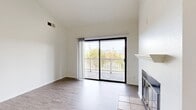 This thoughtfully designed 1-bedroom, 1-bathroom residence offers a bright and functional single-floor layout. The living room serves as the centerpiece of the home, featuring vaulted ceilings that amplify the sense of space, a classic fireplace with a tiled hearth and white mantel, and wood-look flooring throughout. A large sliding glass door opens to a private balcony, framing views of palm trees, lush greenery, and distant mountains, and filling the room with abundant natural light. A pendant light fixture marks the transition into the dining area, which flows seamlessly toward the kitchen. The kitchen is efficiently laid out with white cabinetry, a warm stone-toned countertop, tile flooring, and a full suite of white appliances including a range, microwave, refrigerator, and dishwasher. A window above the sink adds additional natural light. The bedroom is a comfortable retreat, carpeted for warmth, with its own sliding glass door leading to a balcony with scenic outdoor views and a dedicated closet. The bathroom features a vanity with a stone-toned countertop, a shower-tub combination, wood-look flooring, and a high transom window. A hallway and additional closet complete the practical layout of this well-lit, move-in ready home.