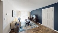 This single-floor residence offers a thoughtfully designed layout that balances functionality and style. The living room serves as the heart of the home, highlighted by a bold navy accent wall, wood-look flooring, and a sliding glass door that invites natural light and provides outdoor access. The space flows seamlessly into a dedicated dining area, which features a pendant light fixture overhead, a second navy accent wall, and neutral tones that create an inviting atmosphere for entertaining.

The kitchen is equipped with dark espresso cabinetry, granite-style countertops, and black appliances including a gas range. A peninsula with a waterfall countertop edge connects the kitchen to the adjoining living and dining spaces, enhancing the open feel of the layout.

Two carpeted bedrooms offer comfortable retreats, each featuring textured ceilings and ample closet space. One bedroom includes a built-in reach-in closet, while the other provides access to an adjoining area. The bathroom includes a full-size soaking tub with clean white surround.

A dedicated laundry area houses a full-size side-by-side washer and dryer, complemented by shelving for additional storage. Wood-look flooring runs throughout the main living areas, tying the overall design together cohesively.