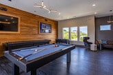 Located at 1980 Icon Way in Knoxville, Tennessee, this single-floor recreation and entertainment facility is thoughtfully designed to deliver a premium leisure experience. The space is defined by its modern aesthetic, blending warm wood accents, dark flooring, and bold design elements throughout.

The game room serves as a central hub, showcasing a striking cedar wood accent wall that frames dual mounted televisions. A full-size pool table and foosball table anchor the room, while large windows flood the space with natural light and offer scenic views of the surrounding landscape. Comfortable seating areas feature a tufted leather sofa positioned against a deep charcoal accent wall, complemented by high clerestory windows that allow additional natural light.

A dedicated golf simulator suite provides a high-tech experience, complete with a large projection screen, putting green turf, and a dramatic geometric-patterned feature wall in blue and taupe that adds bold visual interest. The space is outfitted with golf equipment storage and specialized low-level accent lighting.

The kitchenette is fitted with rich wood cabinetry, light countertops, a stainless steel sink, and open floating shelves styled with greenery and decorative objects. A modern staircase with sleek cable railings connects to the space, lined with curated artwork illuminated by individual picture lights, further reinforcing the refined and contemporary character of this exceptional facility.