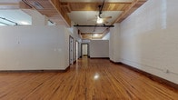 This distinctive loft-style space showcases an impressive blend of industrial charm and functional design across a single, well-appointed floor. Rich, warm hardwood floors run throughout, complementing the painted exposed brick walls that lend an authentic, historic character to every room. The main living area is expansive and open, highlighted by a striking wood-paneled ceiling with structural beams, a ceiling fan, and a black industrial-style track lighting rail that adds a modern edge to the classic backdrop.

Large multi-pane windows flood the interior with natural light, offering views of mature trees outside and creating a bright, airy atmosphere. The kitchen is thoughtfully designed with rich dark wood cabinetry, black appliances, a butcher block island countertop, and an exposed brick chimney column that serves as a dramatic focal point. The space includes two bathrooms — one featuring a full tub and shower with hardwood flooring, and another with rich wood trim accents and a glass partition.

Additional rooms provide flexible use, each benefiting from generous window arrangements and the same warm hardwood floors. The overall ambiance is one of refined, urban character — an inspiring environment where historic architectural elements are seamlessly integrated with contemporary finishes.