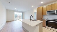 Located at 1028 Stitch Bend Way in Charlotte, NC, this well-appointed single-floor residence offers 1 bedroom and 2 full bathrooms within a thoughtfully designed layout. The open-concept kitchen and living area serves as the heart of the home, anchored by a large center island with a white quartz countertop and a matte black faucet. The kitchen is outfitted with warm wood cabinetry, a white subway tile backsplash, and stainless steel appliances including a refrigerator, range, and microwave. Light hardwood flooring runs throughout the entire unit, lending warmth and continuity to every room. The living area flows seamlessly toward sliding glass doors that open to a private balcony, filling the space with natural light and offering views of the surrounding Charlotte cityscape. The bedroom is a calm, well-lit retreat featuring large windows with urban views and a ceiling fan. Two generously sized walk-in closets provide ample storage. Both bathrooms are finished in a clean, contemporary style with white vanities, matte black hardware, subway tile surrounds, and glass-enclosed showers. Recessed lighting throughout completes the modern aesthetic of this bright, move-in-ready Charlotte residence.