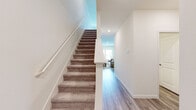 This two-story space combines clean, contemporary design with functional living across multiple well-appointed areas. The main level is anchored by light wood-look flooring that flows seamlessly through the living, dining, and kitchen spaces, creating a cohesive and inviting atmosphere throughout.

The kitchen features white shaker-style cabinetry with brushed nickel hardware, granite countertops, and stainless steel appliances including a range and over-the-range microwave. The adjacent dining area is bright and airy, benefiting from a large sliding glass door dressed with vertical blinds that allows abundant natural light and outdoor views to fill the room.

The living area offers generous proportions with multiple windows that frame outdoor scenery, while neutral walls and warm flooring establish a welcoming ambiance. A full bathroom on one level features wood-look tile flooring, a white vanity, and a tub-shower combination, maintaining the clean, neutral aesthetic found throughout.

Upstairs, the bedroom is a calm retreat with plush carpeting, neutral walls, and a pair of windows that invite natural light and outdoor views. The carpeted staircase, fitted with a sleek handrail, connects the two floors efficiently while complementing the overall design palette.