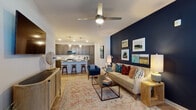 This single-story residence is designed with an open-concept layout that seamlessly connects the living area to the kitchen, creating a cohesive and functional flow. The living room serves as a focal point, highlighted by a bold navy accent wall adorned with a curated gallery of framed artwork. A ceiling fan overhead and light wood-style flooring underfoot add both practicality and warmth to the space. A dedicated media wall provides additional functionality on the opposite side of the room.

The kitchen is well-appointed with dark, shaker-style cabinetry reaching toward the ceiling, white quartz countertops, a subway tile backsplash, and stainless steel appliances. A peninsula with bar seating offers a casual dining option and reinforces the open connection between the kitchen and living areas.

The bedroom features soft, muted tones, a ceiling fan, and direct access to a spacious walk-in closet equipped with dual wire shelving systems and wood-style flooring. The bathroom is finished with a dual-sink vanity featuring dark cabinetry, white quartz countertops, and large rectangular mirrors, maintaining the cohesive design language found throughout the residence.