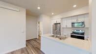 This single-floor residence offers a clean, contemporary design highlighted by light wood-style flooring and a neutral, warm color palette throughout. The open-concept kitchen serves as a central feature, anchored by a large peninsula island with a white quartz countertop and an integrated stainless steel sink. Crisp white shaker-style cabinetry with matte black hardware lines the walls, complemented by a full suite of stainless steel appliances including a refrigerator, electric range, and over-the-range microwave. A dedicated in-unit laundry closet with a stacked washer and dryer is conveniently accessible from the kitchen area. The living area is generously proportioned, bathed in natural light from multiple windows that offer views of surrounding greenery, and is served by recessed lighting overhead. The bedrooms continue the bright, airy feel with large windows and ample wall space. The bathroom is finished with a white quartz vanity, white shaker cabinetry with matte black hardware, a large mirror, and stylish pendant lighting. Throughout the unit, the consistent use of clean finishes and thoughtful design creates a cohesive, move-in-ready living environment.