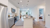 Located at 1170 Temple Dr in Sugar Hill, GA, this single-floor residence offers a thoughtfully designed open-concept layout that seamlessly connects the kitchen, dining, and living areas. The kitchen is a standout feature, equipped with stainless steel appliances, granite countertops, two-tone white and gray cabinetry, a subway tile backsplash, and a large island with bar seating illuminated by globe pendant lights. Light wood-look flooring extends throughout the main living areas, enhancing the bright and airy atmosphere created by recessed lighting and large windows that invite natural light. The living room makes a bold design statement with a striking green vertical batten accent wall, serving as a rich backdrop to the space. A stylish chandelier and generous window placement further elevate the room's character. The bedroom is a calm retreat featuring plush carpeting, a large window with outdoor views, and access to a spacious walk-in closet with wrap-around rods and ample storage. The bathroom continues the refined aesthetic with granite countertops, gray cabinetry with modern hardware, an undermount sink, and built-in shelving. Every detail of this residence reflects a contemporary design sensibility with high-quality finishes throughout.