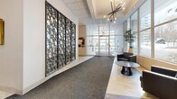 Located at 565 Avenue Rd in Toronto's prestigious Forest Hill neighbourhood, this building lobby offers a polished and welcoming first impression. The space is defined by a refined architectural layout that guides visitors from the main entrance through to the elevator bank with a clear, functional flow.

A standout feature is the large, full-height decorative screen panel composed of interlocking circular motifs, serving as a bold artistic focal point along one wall. Overhead, striking sputnik-style chandeliers hang from a coffered ceiling with crown moulding detail, lending a mid-century modern elegance to the space. Recessed lighting throughout provides supplementary illumination, ensuring the lobby is bright and inviting at all hours.

Floor-to-ceiling windows along the entrance facade flood the interior with abundant natural light, offering views onto Avenue Road and creating an open, airy ambiance. The flooring transitions between polished tile and a central carpet runner, adding visual structure and warmth to the corridor.

A seating area with sleek, dark upholstered furniture and a contemporary round coffee table provides a comfortable waiting space for visitors. Curated artwork is displayed prominently on the walls, contributing to a gallery-like atmosphere. Adjacent to the elevator bank, tile surrounds and textured wall finishes add further architectural interest, completing a lobby that balances sophistication with practicality.