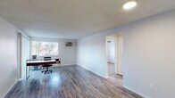 This single-floor unit is designed with a practical, open layout that maximizes usable living space. The main living area features durable hardwood-style flooring and neutral gray-toned walls, creating a bright and airy atmosphere. A sliding glass door opens to a private balcony, allowing natural light to fill the room while providing outdoor access. Baseboard heating ensures comfortable temperatures throughout the year.

The kitchen is thoughtfully appointed with gray cabinetry, white quartz-style countertops, and a classic white subway tile backsplash. Black appliances, including an electric range and refrigerator, complement the modern aesthetic, while light hardwood-style flooring ties the space together seamlessly.

The bedrooms are carpeted for comfort and include windows with blinds that provide natural light and outdoor views. One room features a wall-mounted air conditioning unit and a textured ceiling, while another includes a ceiling fan with a built-in light fixture and baseboard heating. The bathroom is well-appointed with a tiled tub-surround shower, updated gray vanity with an integrated sink, and wood-style flooring. Throughout the unit, textured ceilings add a classic finish to each room.
