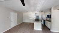 This single-floor residence offers a clean, modern aesthetic with a thoughtfully designed open-concept layout. Durable wood-style flooring flows consistently throughout the home, providing a cohesive and low-maintenance foundation in every room.

The living area is bright and welcoming, featuring a ceiling fan with light fixture, a textured ceiling, and a large sliding glass door dressed with vertical blinds that allows generous natural light to fill the space. A private entry door adds convenience and accessibility directly from the living area.

The kitchen is efficiently laid out in a galley style, opening toward the main living space via a peninsula counter with stone-look countertops. It is equipped with stainless steel appliances including a refrigerator and range, a white refrigerator, a dishwasher, and a stacked washer/dryer unit. Track lighting overhead provides ample task illumination.

The two bedrooms are quiet and comfortable, each finished with the same wood-style flooring and neutral warm-toned walls. One bedroom features a sleek ceiling fan, while the other benefits from a bright window with horizontal blinds, allowing natural light to filter in. Both rooms offer a clean, versatile canvas suitable for a variety of furnishing arrangements.

Overall, this residence presents a practical and modern living environment with consistent finishes and functional design throughout.