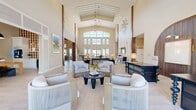 Located at 2950 Landover Blvd in Spring Hill, Florida, this single-floor community clubhouse offers a generously sized, thoughtfully designed gathering space with a distinctly coastal aesthetic. The centerpiece of the facility is a dramatic grand lounge boasting soaring vaulted ceilings with coffered detailing, a striking floor-to-ceiling palm tree mural on a shiplap accent wall, and an abundance of natural light streaming through expansive upper-level windows and glass entry doors. Light wide-plank hardwood flooring flows throughout, complementing the warm, neutral color palette. Rich dark wood structural columns frame the open-plan layout, creating natural zones for socializing and relaxation. A dedicated coffee bar area — branded as Trapeze — features a stylish service cart, pendant lighting with woven rattan shades, upholstered seating, and banquette-style dining. An additional lounge area with bar-height seating is set against a textured stone accent wall with pendant lighting. A spacious flex room with high ceilings and botanical artwork provides further versatile gathering space. A dedicated mailroom with floor-to-ceiling individual mailboxes, stone tile flooring, and decorative patterned wallcovering rounds out the facility. The overall ambiance is airy, refined, and welcoming.