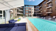 This expansive outdoor pool area is nestled within a modern, multi-story residential community, creating a vibrant courtyard environment that is open to the sky and bathed in natural sunlight. The centerpiece is a generously sized swimming pool with crystal-clear blue water, complemented by a wide surrounding deck outfitted with rows of white lounge chairs and stylish blue upholstered seating, ideal for relaxing and socializing.

The space is thoughtfully designed with multiple amenity zones. An outdoor grilling station with a granite countertop provides a convenient setup for al fresco dining, while a dedicated area features a ping-pong table for recreational use. Shaded seating with market umbrellas offers a comfortable respite from the sun. Decorative ornamental grasses and carefully placed planters add natural texture throughout the space.

A standout architectural feature is a large water wall finished in vibrant iridescent mosaic tiles in a kaleidoscope of blues, purples, and warm tones, creating a visually striking focal point at one end of the courtyard. Water cascades gently down its surface, adding both movement and ambiance. The surrounding building facades, featuring contemporary materials including brick, steel-railed balconies, and large windows, frame the courtyard and contribute to the polished, modern aesthetic of the overall environment.