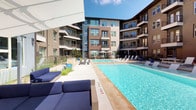 This expansive outdoor pool area is nestled within a modern, multi-story residential community, creating a vibrant courtyard environment that is open to the sky and bathed in natural sunlight. The centerpiece is a generously sized swimming pool with crystal-clear blue water, complemented by a wide surrounding deck outfitted with rows of white lounge chairs and stylish blue upholstered seating, ideal for relaxing and socializing.

The space is thoughtfully designed with multiple amenity zones. An outdoor grilling station with a granite countertop provides a convenient setup for al fresco dining, while a dedicated area features a ping-pong table for recreational use. Shaded seating with market umbrellas offers a comfortable respite from the sun. Decorative ornamental grasses and carefully placed planters add natural texture throughout the space.

A standout architectural feature is a large water wall finished in vibrant iridescent mosaic tiles in a kaleidoscope of blues, purples, and warm tones, creating a visually striking focal point at one end of the courtyard. Water cascades gently down its surface, adding both movement and ambiance. The surrounding building facades, featuring contemporary materials including brick, steel-railed balconies, and large windows, frame the courtyard and contribute to the polished, modern aesthetic of the overall environment.