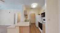 This single-story unit at 10900 E Taylor Rd in Gulfport, Mississippi offers a well-organized layout with a blend of wood-look flooring and plush carpeting throughout. The kitchen is designed for functionality, featuring light wood cabinetry, a raised breakfast bar peninsula that opens to the living area, a double sink, ample counter space, and a full suite of appliances including a refrigerator, electric range, and built-in microwave. Crown molding adds a refined touch to the kitchen and adjoining areas.

The living room is generously sized, finished with soft carpeting and a ceiling fan with light fixture. A set of French doors fills the space with natural light and provides access to the outdoors. A dedicated dining area is illuminated by a hanging chandelier, complementing the open flow between the kitchen and main living spaces.

The bedrooms are carpeted and comfortably proportioned, each equipped with ceiling fans. One bedroom includes a window that allows natural light to filter in. The bathroom is outfitted with a light wood vanity, a wide mirror with overhead lighting, a tub-shower combination, and wood-look flooring. A dedicated laundry area with overhead cabinetry and utility hookups rounds out the practical amenities of this unit.