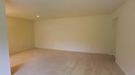 Located at 16A Valley Lake, this single-floor space features a generously sized open room that offers a blank canvas for a variety of uses. The room is finished with neutral-toned walls that create a bright, airy atmosphere, complemented by wall-to-wall carpeting in a warm beige tone that adds softness underfoot. The ceiling follows a subtle slope, adding a modest architectural detail to the otherwise clean, minimalist interior. Recessed lighting is integrated into the ceiling, providing consistent illumination throughout the space. Electrical outlets are conveniently positioned along the walls, supporting practical everyday use. The overall design is simple and understated, emphasizing functionality and versatility. The neutral color palette throughout ensures the space can easily accommodate a range of interior styles and purposes, making it adaptable for prospective occupants looking to personalize the environment to their needs.