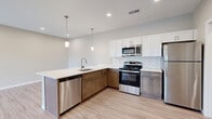 Located at 1154 N Old Castle Rd in Nixa, Missouri, this well-appointed one-bedroom, one-bathroom unit offers a thoughtfully designed single-floor layout that maximizes every square foot. The open-concept kitchen and living area serves as the heart of the home, anchored by a large peninsula with a white quartz countertop, undermount sink, and pendant lighting overhead. The kitchen is outfitted with white shaker upper cabinets, warm-toned lower cabinets, a classic subway tile backsplash, and a full suite of stainless steel appliances including a refrigerator, gas range, microwave, and dishwasher. Light wood-look flooring runs throughout the main living areas, lending a clean and contemporary feel. The living room offers recessed lighting, a ceiling fan, and a glass patio door that invites natural light and outdoor access. The bedroom features plush carpet, a closet with a sliding barn-style door, and a window with outdoor views. The bathroom is finished with a white vanity, quartz countertop, large mirror, and light tile flooring in a neutral palette. A dedicated laundry area with washer/dryer hookups completes the functional layout. Neutral wall tones and modern hardware throughout create a cohesive, move-in-ready aesthetic.