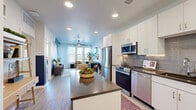 Located on E Colfax Ave in Aurora, Colorado, this well-designed one-bedroom, one-bathroom unit offers a thoughtfully efficient layout across a single floor. The open-concept living and kitchen area creates a seamless flow, anchored by light wood-style flooring and recessed lighting throughout. The kitchen is outfitted with stainless steel appliances — including a range, microwave, and dishwasher — complemented by white shaker cabinetry, dark countertops, a gray tile backsplash, and a movable island for added prep space. The living room is bright and inviting, featuring large windows, a ceiling fan, and direct access to a private balcony with open city views. A bold geometric accent wall in teal and navy adds a distinctive design element visible from both the living area and the bedroom. The bedroom offers a cozy retreat with plush carpet, a large sliding window with outdoor views, and its own geometric accent wall. The bathroom features a wide vanity with dark countertops, white cabinetry, and a large framed mirror. A dedicated closet provides practical storage. The unit combines modern aesthetics with functional design, making it a polished and comfortable urban residence.