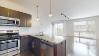 Located at 1240 Chapel St in New Haven, Connecticut, this single-floor residence offers a thoughtfully designed open-concept layout with contemporary finishes throughout. The kitchen serves as a central focal point, featuring dark espresso cabinetry with sleek bar-pull hardware, granite countertops, a central island with an integrated sink and dishwasher, and a full suite of stainless steel appliances including a gas range, microwave, and refrigerator. Pendant lighting above the island and track lighting overhead add both functional and stylish illumination.

The kitchen flows seamlessly into the living area, where wide-plank hardwood-style flooring, crisp white walls, and large sliding glass doors and oversized windows fill the space with natural light and offer views of the surrounding neighborhood, including glimpses of classic New Haven brick architecture. Track lighting continues throughout the main living space.

The bedrooms feature plush carpeting and generous windows with exterior views, creating bright, comfortable retreats. Two full bathrooms are finished with large-format tile flooring, tub-shower combinations with white tile surrounds, and modern vanities with dark cabinetry and clean white countertops. The overall aesthetic is clean, modern, and move-in ready.