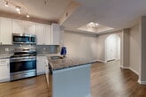 This single-floor residence showcases a thoughtfully designed open-concept layout that seamlessly connects the living and kitchen areas. A striking arched entryway frames the main living space, drawing the eye toward a tray ceiling fitted with track lighting that adds a refined architectural touch. The living room is generously proportioned, featuring rich hardwood-style flooring, a classic fireplace flanked by large windows that allow natural light to pour in, and a ceiling fan for year-round comfort.

The kitchen is well-equipped and functional, boasting white shaker cabinetry, a tasteful subway tile backsplash, granite countertops, and a full suite of stainless steel appliances including a refrigerator, range, and microwave. A peninsula with an undermount sink and additional granite counter space provides both a practical workspace and a casual dining option.

The bedrooms offer a softer, more restful atmosphere with plush carpeting, neutral tones, and ceiling fans. One bedroom features a walk-in closet and access to natural light through a window overlooking a greenery-filled exterior. The bathrooms are finished with granite vanity tops, white cabinetry, wood-look flooring, and tiled tub-shower combinations, completing this cohesive and comfortable residence.