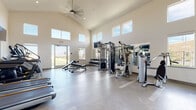 This single-floor fitness center, located in Folsom, CA (95630), offers a bright and spacious workout environment defined by its striking architectural design. The room features soaring vaulted ceilings with clerestory windows lining the upper walls, flooding the space with natural light from multiple directions. A large ceiling fan provides comfortable air circulation throughout the open layout, while neutral-toned walls and polished concrete flooring contribute to a clean, modern aesthetic.

The facility is comprehensively equipped to support a full range of fitness routines. The cardio zone includes multiple treadmills, stationary bikes, and a rowing machine, all positioned in front of wall-mounted flat-screen televisions. A full-length mirror along one wall visually expands the space and aids in form monitoring during workouts. The strength training area features a multi-station cable machine, a dedicated dumbbell rack with a wide weight selection, adjustable benches, and various Hoist-brand selectorized machines including a leg press. Stability balls in multiple sizes are neatly stored on a rack, offering options for functional fitness and core training. A mini-fridge and sanitation station are conveniently available near the entrance. Large glass doors provide access to an outdoor area with green views, enhancing the overall workout atmosphere.