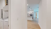 This single-floor unit showcases a clean, modern aesthetic throughout, with light hardwood flooring and crisp white walls creating a bright, cohesive atmosphere. A hallway entrance leads into an open-concept kitchen and living area, where the kitchen stands out with white shaker-style cabinetry, subway tile backsplash, granite countertops, and stainless steel appliances including a refrigerator with ice maker, range, and microwave. Pendant lighting hangs above the granite-topped island, which offers additional prep and seating space. A sliding barn door adds a stylish architectural detail near the kitchen.

The bedrooms are well-proportioned with light-filled windows, ceiling fans, and continued hardwood flooring. One bedroom includes access to a generous walk-in closet fitted with multi-level wire shelving systems for organized storage. Both full bathrooms feature soaking tub and shower combinations with large-format gray tile surrounds, white vanities with granite countertops, and hardwood-style flooring. A dedicated laundry area houses a full-size top-loading washer and wire shelving. The overall design prioritizes functionality and modern finishes throughout.