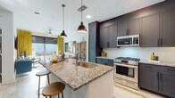 This single-floor residence is thoughtfully designed with a cohesive blend of modern finishes and bold, eclectic décor. The open-concept kitchen serves as the heart of the space, anchored by a large granite-topped island with an undermount sink and seating for casual dining. Dark gray shaker-style cabinetry extends to the ceiling, complemented by a white tile backsplash and a full suite of stainless steel appliances, including a gas range, over-the-range microwave, and a French door refrigerator. Pendant lighting above the island adds a stylish focal point. Light wood-look flooring flows throughout the main living areas, connecting the kitchen seamlessly to the living room. The living area is bright and inviting, featuring floor-to-ceiling sliding glass doors draped in golden yellow curtains that allow natural light to pour in. A curated gallery wall, a ceiling fan, and vibrant furnishings give the space a lively, artistic character. The bedroom continues the bold aesthetic with a teal upholstered headboard, floral curtains, sliding glass door access, and soft carpet underfoot. The en-suite bathroom offers granite countertops, dark cabinetry, and direct access to a dedicated walk-in closet, completing this well-designed and visually dynamic residence.