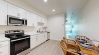 Located at 5310 Adobe Falls Rd in San Diego, CA, this efficiently designed one-bedroom, one-bathroom unit offers a clean, modern aesthetic throughout its single-floor layout. Light wood-style vinyl flooring flows continuously through the space, complementing the bright, neutral wall tones that enhance the sense of openness.

The kitchen is thoughtfully appointed with crisp white shaker cabinetry featuring brushed nickel hardware, white quartz countertops, and a full suite of stainless steel appliances including an electric range, built-in microwave, and dishwasher. Recessed lighting illuminates the workspace, which opens directly to a dining area furnished with woven rattan seating.

The generously proportioned bedroom is one of the unit's standout features, accommodating a full sleeping area with room to spare. Two large windows invite abundant natural light and frame scenic views of the surrounding hillside. A wall-mounted flat-screen TV and a sliding-door closet complete the room.

The bathroom maintains the same clean, contemporary palette with white shaker vanity cabinetry, a wide rectangular mirror, quartz countertop, and a shower-tub combination. Recessed and vanity lighting ensure a well-lit, functional space. Overall, the unit presents a cohesive, move-in-ready environment with modern finishes throughout.