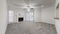 Located at 1816 S Carson Ave in Tulsa, Oklahoma, this single-story residence offers a well-organized and functional layout throughout. The living room serves as the heart of the home, featuring plush carpeting, crown molding, a ceiling fan with light fixture, and a tile-surround fireplace with a classic white mantle. Vertical blinds cover a sliding glass door that opens to the outside, allowing natural light to filter in. The kitchen is efficiently designed with warm oak cabinetry, dark granite-style countertops, and black appliances including a refrigerator, electric range, microwave, and dishwasher. Wood-look vinyl plank flooring completes the kitchen's practical aesthetic. The bedrooms are carpeted and bright, with ceiling fans and window blinds providing comfort and light control. One bedroom features a walk-in closet with built-in shelving and hanging rods, offering generous storage. The bathroom includes an oak vanity with a dark granite countertop, a large wall mirror, and a tub-shower combination. Textured ceilings are found throughout the home, contributing to its consistent interior character. The space presents a clean, neutral palette well-suited for a variety of living arrangements.