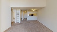 This single-level, two-bedroom, one-bathroom residence follows a Plan D layout designed for functional, comfortable living. The living room serves as the heart of the home, featuring a tile-surround fireplace, plush carpeting, and a large arched sliding glass door fitted with vertical blinds that allow abundant natural light and outdoor access. A ceiling fan adds to the room's comfort. Built-in shelving along one wall provides convenient display and storage space.

The kitchen is positioned in an open-concept arrangement, visible from the living area. It is equipped with stainless steel appliances, including a refrigerator and microwave, as well as warm wood-toned cabinetry and granite-style countertops. A dishwasher and stovetop are also included. The kitchen's layout offers easy flow into the adjoining living and dining areas.

Both bedrooms are carpeted and feature vertical blinds over windows that bring in natural light. Baseboard heating is present in each bedroom, ensuring year-round comfort. The single full bathroom includes a tub/shower combination with sliding glass doors, a wood-vanity with a granite-style countertop, and tile flooring. A small window near the ceiling provides ventilation and additional light.