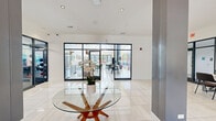 Located at 860 W Panorama Dr in Palatine, IL, this single-floor community clubhouse offers a well-rounded amenity space designed for both relaxation and productivity. The welcoming entrance lobby features polished large-format tile flooring, a sculptural glass-top accent table, and a sputnik-style chandelier, establishing a clean, contemporary aesthetic throughout.

The central lounge area is anchored by a sleek linear fireplace set against a dark feature wall, complemented by rounded upholstered seating, copper pendant lighting, and a striking arched window that frames lush outdoor greenery. Adjacent to the lounge is a bright, airy co-working and social space with soaring vaulted ceilings, floor-to-ceiling glass doors opening to the exterior, and a bold large-scale mural providing a vibrant focal point. Long communal tables and mixed seating arrangements make this area well-suited for both casual gatherings and focused work.

A dedicated business nook offers a workstation desk, coffee station, and an elegant arched window overlooking the landscaped grounds. The full-sized fitness center is equipped with Life Fitness cardio machines, strength equipment, and mirrored walls beneath an industrial-style open ceiling. A separate yoga and movement studio features hardwood-style flooring, full-wall mirrors, mounted displays, and generous natural light from large windows — ideal for group classes or individual practice.